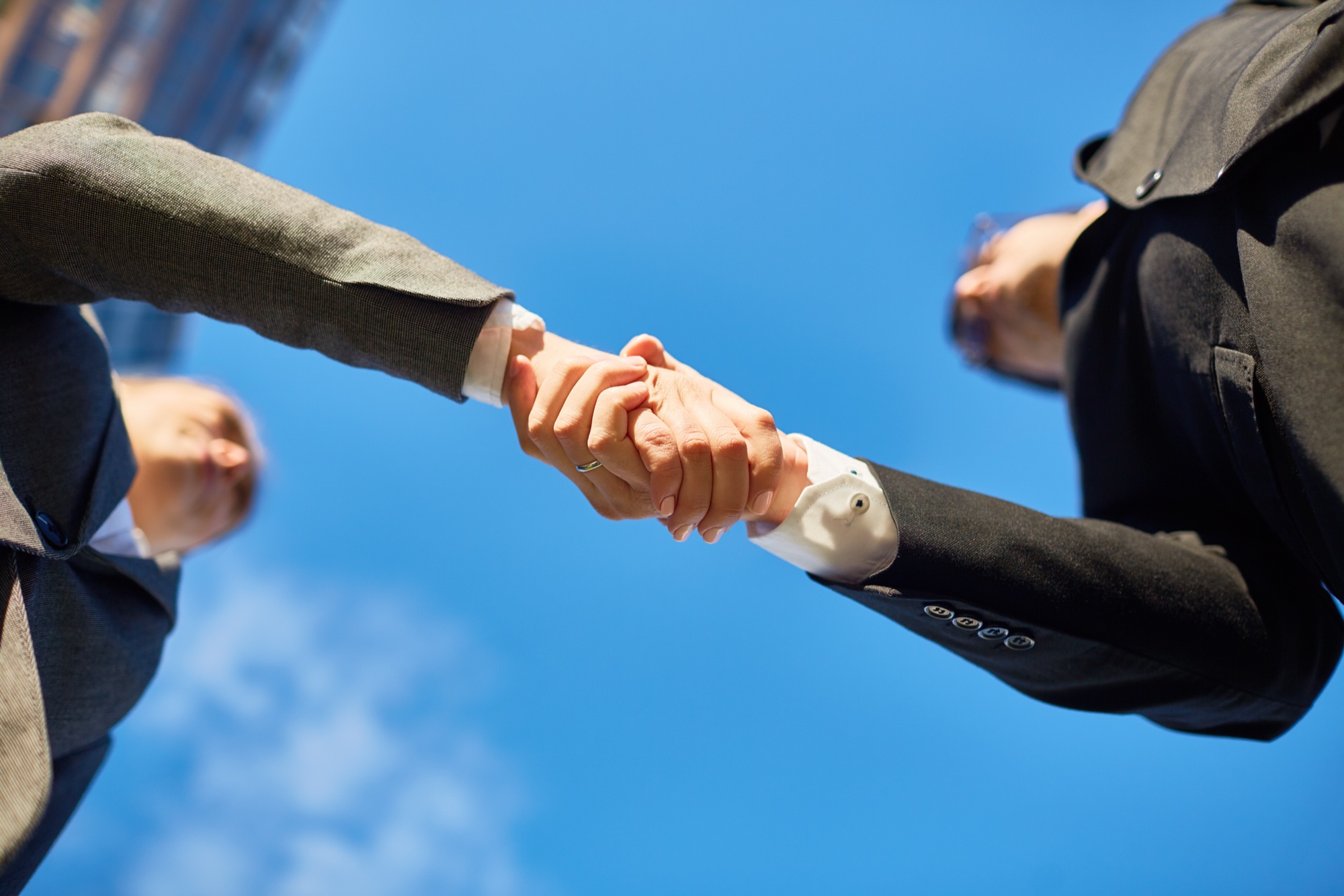 Business partners shaking hands under blue sky